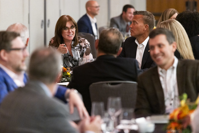 People seated at round tables engaged in conversation during an event.