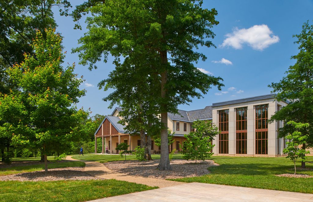 Exterior view of a campus building surrounded by trees and pathways on a sunny day, with tall windows and a mix of modern and traditional architectural design.