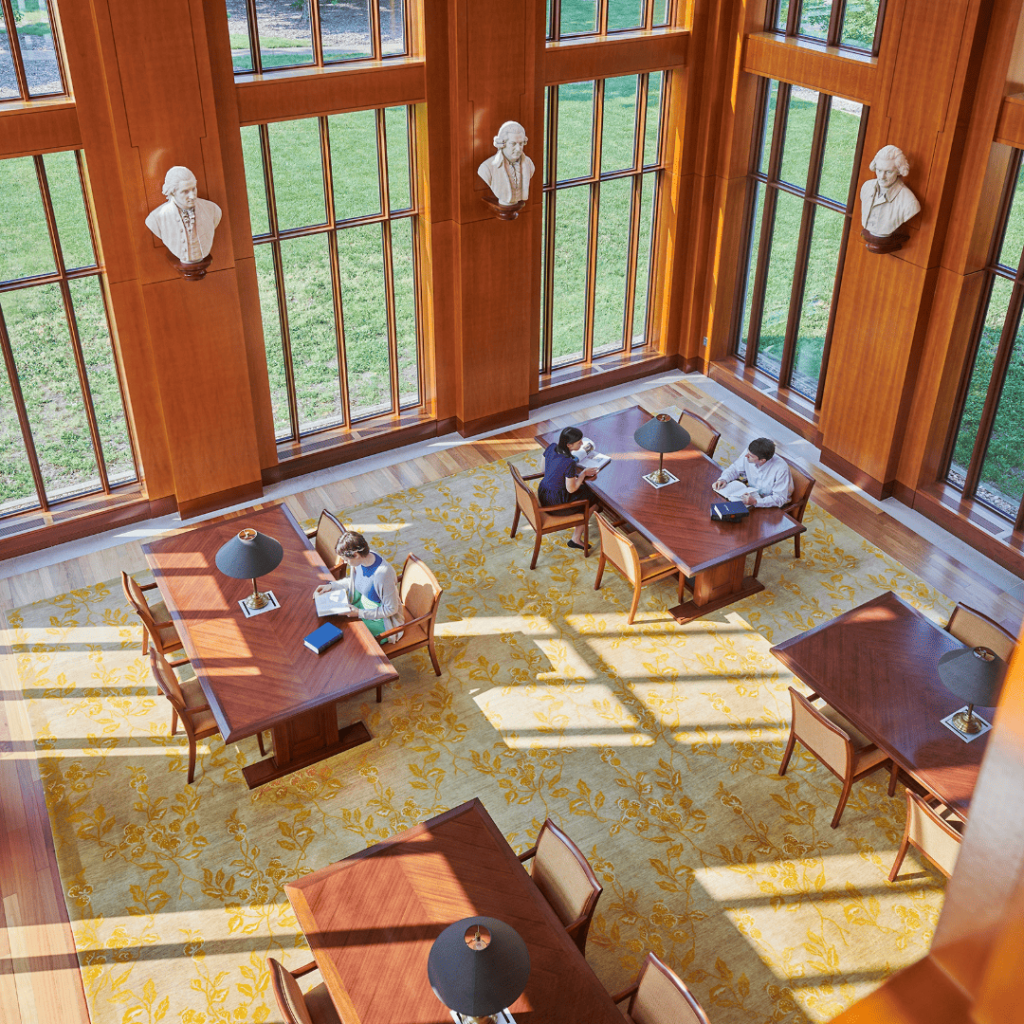 Library with tall windows, busts on walls, and people studying at wooden tables.