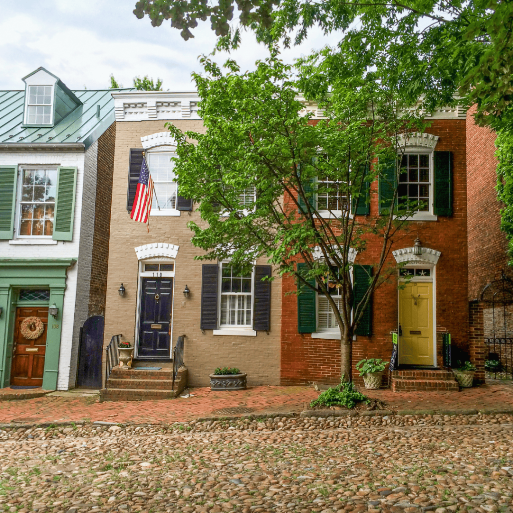 Row of colorful historic brick townhouses with shutters and cobblestone street.
